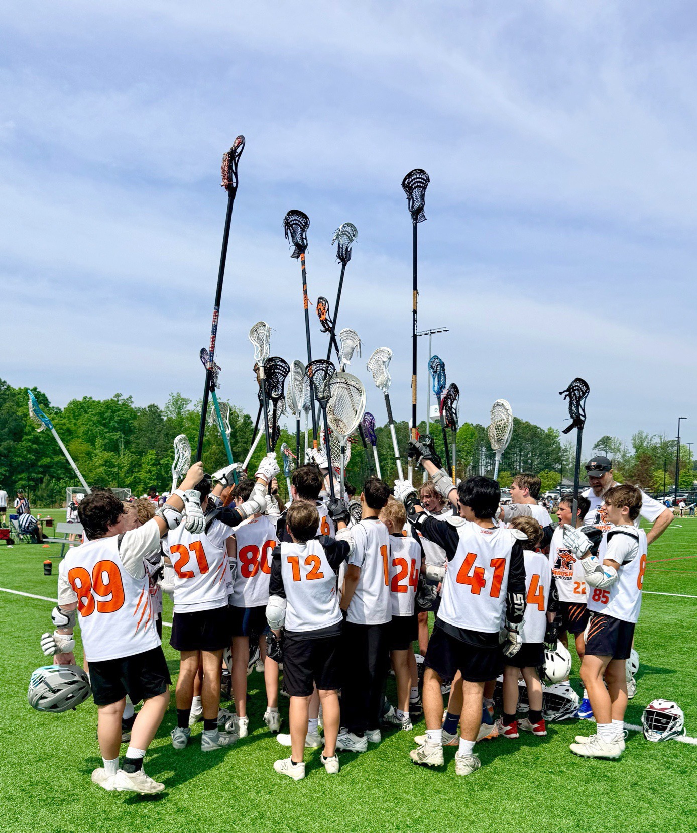 Ambush Lacrosse youth players raising their lacrosse sticks after a game